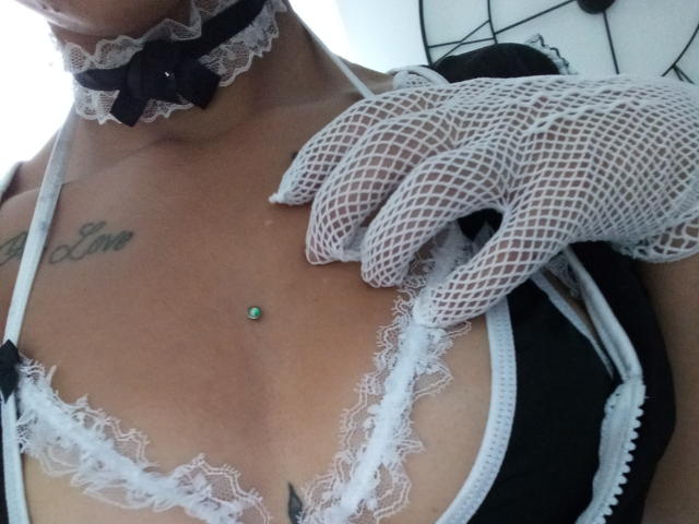 De gebruinde huid van KassiKassou, de zwarte en witte kanten BH, de witte nethemdshandschoenen, de zwarte choker met kant, de kleine groene piercing in de tepel, de tatoeage op de rechterborst en de tatoeage op het linker sleutelbeen..