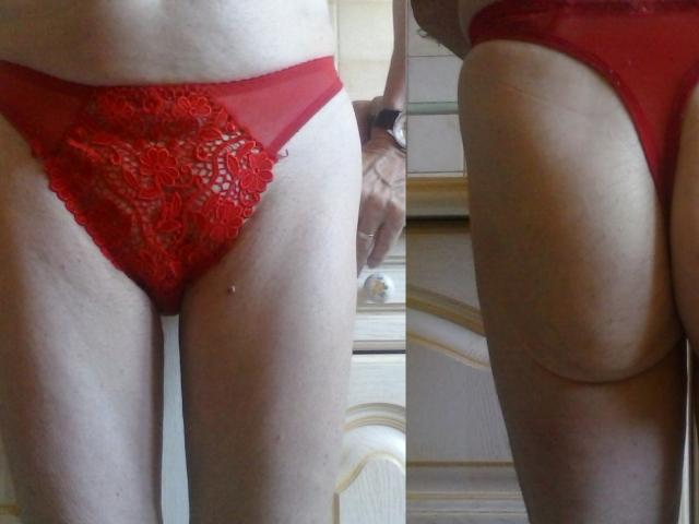 As calcinhas vermelhas de renda de Hermeline, com parte frontal transparente e um padrão intrincado, são mostradas de dois ângulos, destacando sua pele clara e a vulva visível através do tecido..