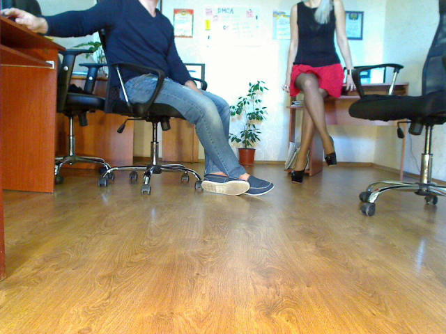 PassionateBlonde in a black top and red skirt sits with legs crossed, showing off her ass in black heels. Another PassionateBlonde in a black top and blue jeans sits.