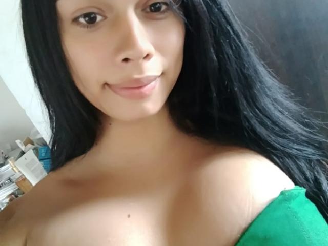ValeriaHot69TS has long black hair, brown eyes, and a small smile. She's topless with green fabric covering her tits, showing a cute mole on her chest.