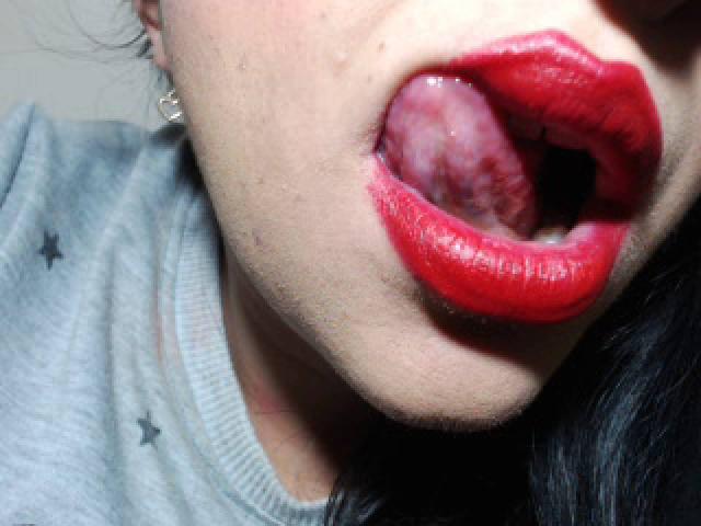 LuluFrancaise's mouth is open wide, tongue out, with bright red lipstick and slightly parted pink lips. She's wearing a gray shirt with small star patterns.