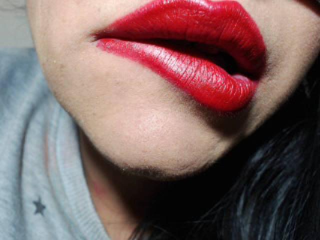 LuluFrancaise's glossy red lips are plump and shiny, with visible lip texture. She's wearing a gray shirt, and her black hair is partially visible.