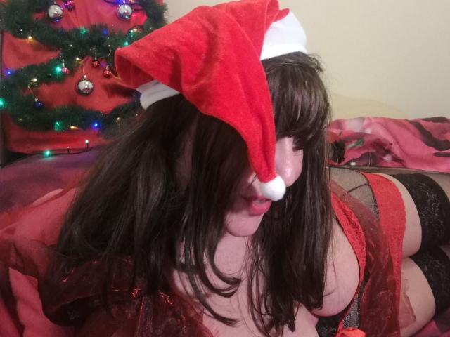 Monellina with red Santa hat, brown hair, red lace lingerie, black garter, and red sheer robe, showing her tits and ass, on a bed with Christmas lights.
