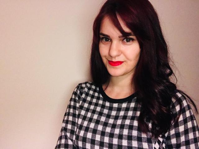 LaraFontaineX with red lipstick, black and white checkered shirt, and dark wavy hair, smiling slightly, showing her nose ring. Her tits are average-sized and she has a cute face.