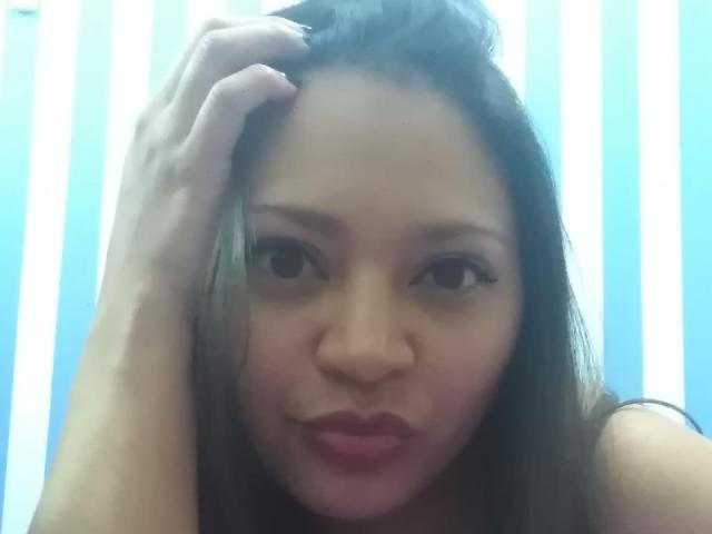 DakotaSweet tiene ojos marrones, cabello lacio y castaño, y está frunciendo los labios. Está sujetando su cabello con la mano derecha, mostrando su nariz y sus labios rosados ligeramente entreabiertos..