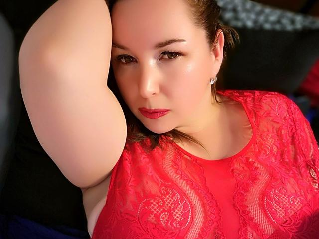 TitanicTits with fair skin, red lace top, and red lipstick, raising arm, looking at camera, brown eyes, earrings, brown hair, slightly flushed face, sexy, confident.