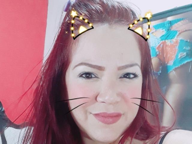 KarolSexxy with red hair, cat ears, and whiskers, smiling, pink lips, black eyeliner, and fair skin, showing her nose and cute face. Boobs not visible.