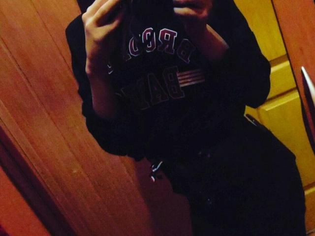 DanceErika's reflection shows her in a dark shirt, holding a phone, with her hands near her chest. She's wearing black pants, and the image is slightly blurry.