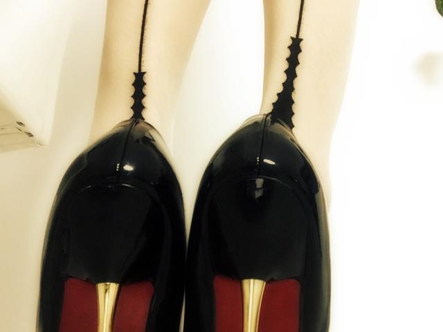 MistressOfShadow's shiny black stiletto heels with red soles and golden tips, showing her bare, pale legs and the black straps running up her ankles.