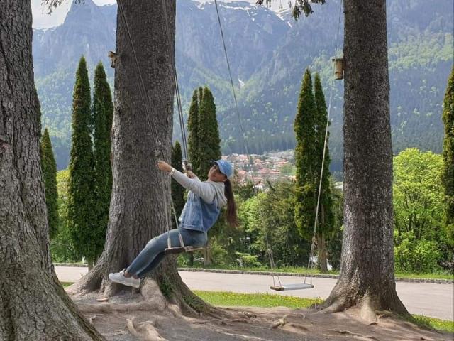 DashingFoxyX is swinging from a rope in a forest, wearing a blue hoodie, denim vest, and jeans, with a mountain and trees in the background.