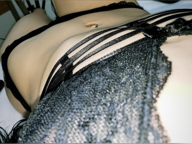 Le bas du dos et les fesses de LexyJensen sont visibles, vêtus de lingerie en dentelle noire avec des détails à bretelles, et elle a un piercing argenté au nombril. Le bas de sa lingerie en dentelle grise est partiellement visible..