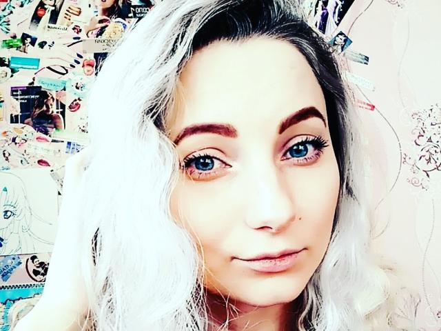 JillFox, com cabelo branco, olhos azuis e sobrancelhas grossas, sorrindo levemente, mostrando seu nariz e lábios. Seus seios não são visíveis nesta foto..