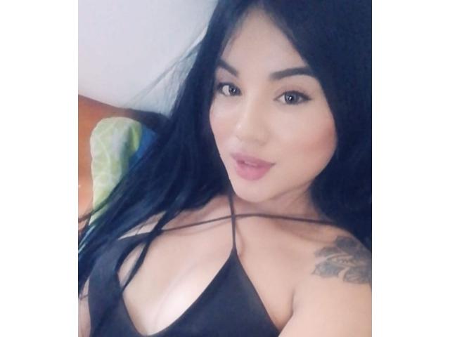 SteffanyTaylor with long black hair, wearing a black halter top, showing her tits, tattoo on right shoulder, light makeup, slightly parted lips, looking at camera.