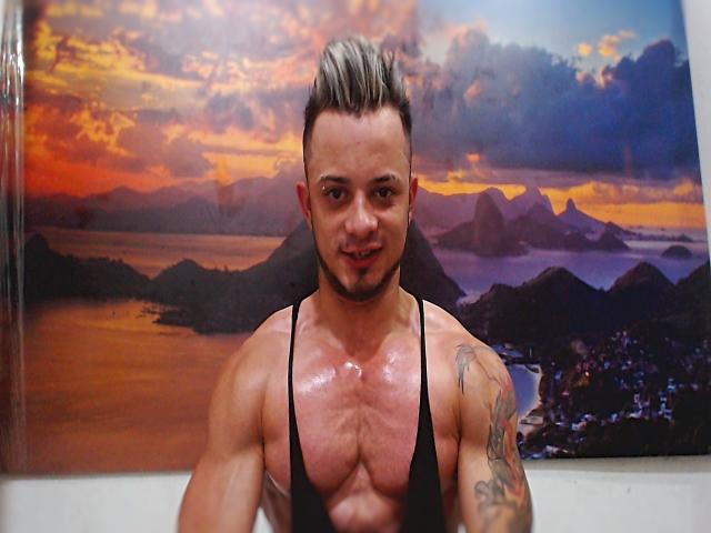 Everet, muscoloso, con un tatuaggio sul braccio destro, pelle liscia e una canotta nera, sorride alla fotocamera. Ha un taglio di capelli con punte e striature grigie..