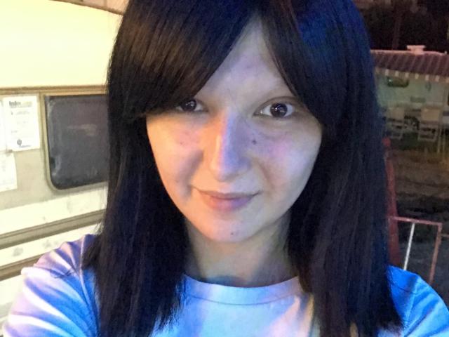 AmethystCharm has straight black hair, brown eyes, and a slight smile. She's wearing a white shirt, with a light blue glow on her right side.