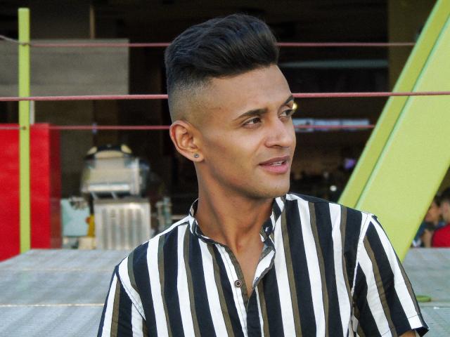 Antonnii has short, styled black hair, a clean-shaven face, and is wearing a black-and-white striped shirt. He's looking to the side with a slight smile.