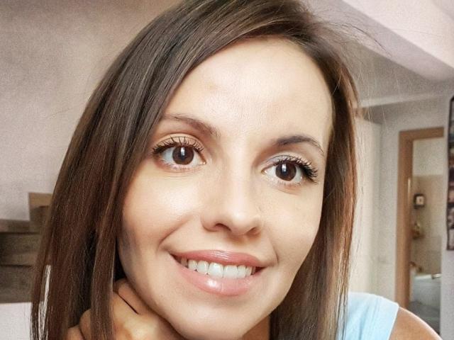 MissJoliSourireBg ha gli occhi marroni, i capelli castani lisci e un sorriso carino con labbra rosa lucide. Sta guardando la fotocamera con un leggero rossore sulla guancia..