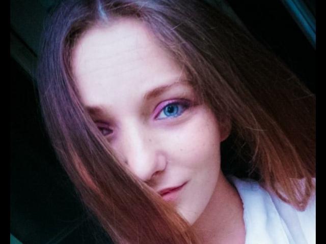 DannaShiny hat ein süßes Gesicht mit blauen Augen, hellbraunen Haaren und einem leichten Lächeln. Sie trägt ein weißes Hemd, und ihre Nase ist klein..