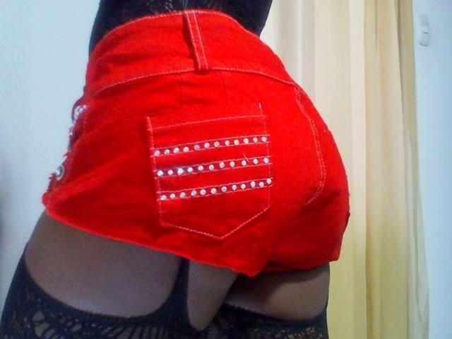 LaylaXimena69's red denim shorts with white studded pockets, butt facing camera, black lace stockings, slightly visible butt crack, against a white wall.