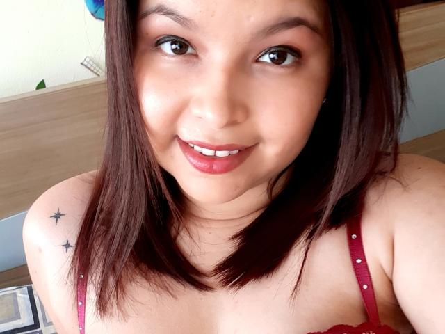 Myalewwis with brown hair, red lipstick, and red bra, showing small tits, star tattoo on shoulder, smiling at camera, light skin, and slight freckles.