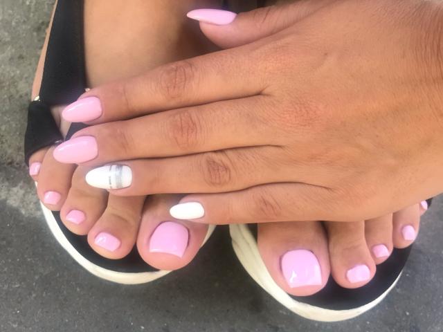 Jenniferwild69's hands with pink nail polish, one white nail, and a silver ring, resting on her pink-toenailed feet in black flip-flops.