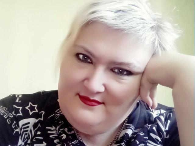 LanaNighty with short, messy blonde hair, red lipstick, and black star-patterned shirt, resting her head on her hand, looking at the camera with a slight smile.