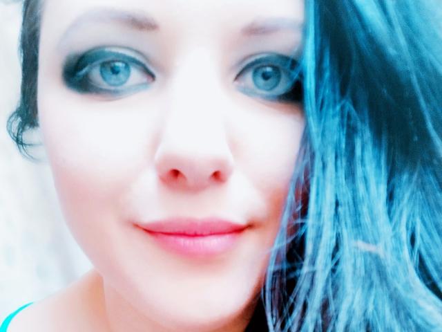 Un selfie di SweetttAngel con occhi azzurri, eyeliner scuro, labbra rosse e capelli blu che le coprono metà del viso. Sorride leggermente, con un'espressione dolce e tenera..
