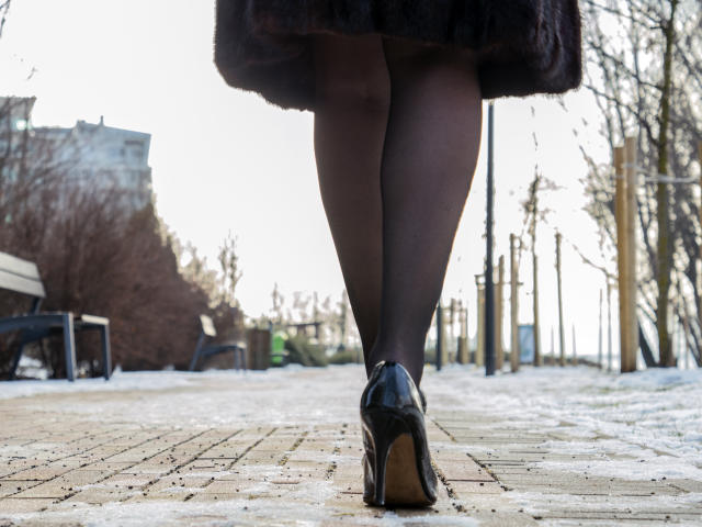 MistressLaurie's black pantyhose and shiny black heels, standing with her ass slightly visible, on a snow-dusted brick path, wearing a dark fur coat, back to the camera.