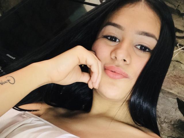 CelesteEvanss has long black hair, full pink lips, and a tattoo on her left wrist. She's looking at the camera with her hand near her face, showing off her tits.
