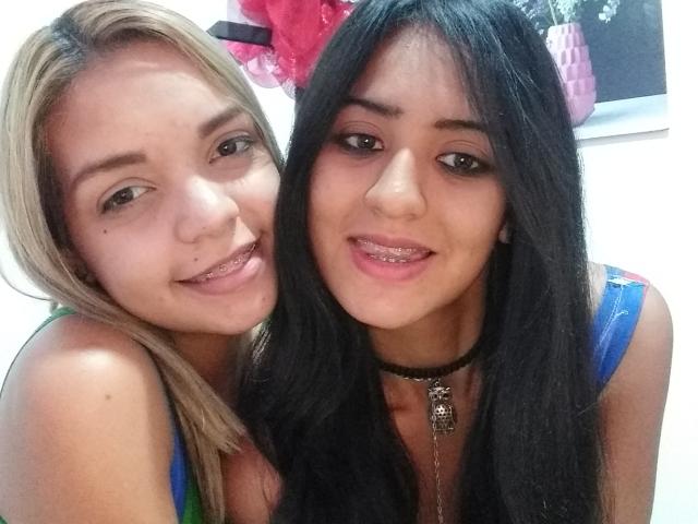 Due WannaPlayWithMe, una con i capelli biondi e l'altra con i capelli neri, entrambe sorridenti con le labbra rosa e che indossano top blu. La WannaPlayWithMe bionda ha una piccola lentiggine sulla guancia..