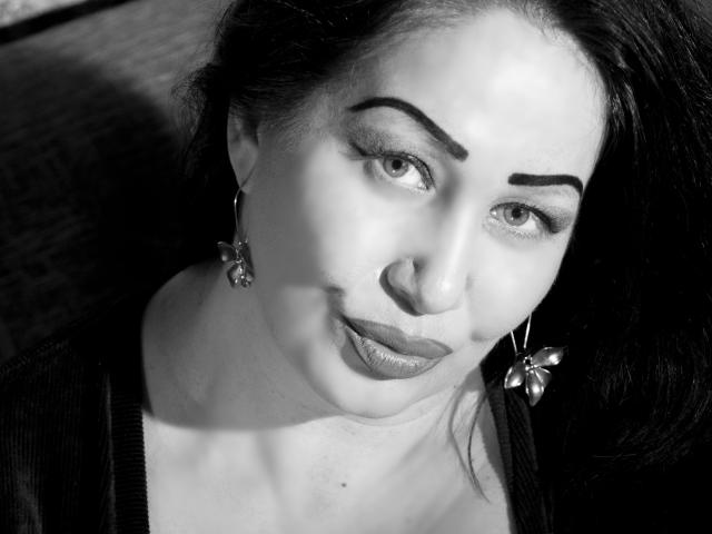 LexyRose has dark, thick eyebrows, wearing butterfly earrings, and looking up with a slight pout, showing her shiny, plump lips and smooth, fair skin in a black-and-white photo.
