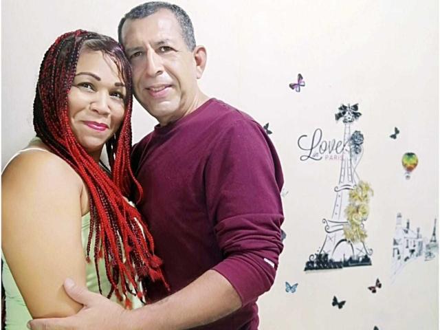 PamelaYDiego, con cabello rojo trenzado, senos medianos y piel clara, abraza a un hombre con cabello corto, trasero de tamaño medio y piel bronceada, que lleva una camisa roja de manga larga..