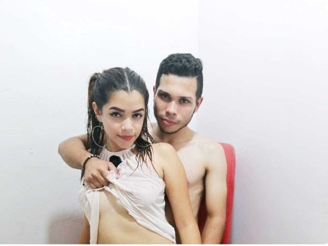 Stefany y Juan, con el pelo mojado, ella levantando una camisa blanca para mostrar sus pechos, de pie frente a Juan, que está sin camisa, con un brazo alrededor de ella, en una habitación blanca..