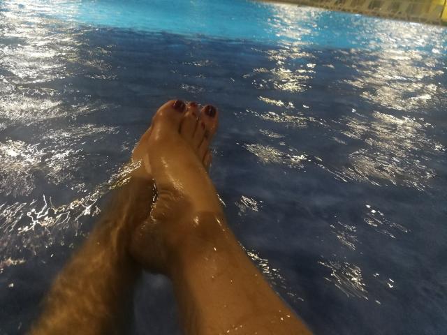 Angelonix's wet foot with brown toes, slightly hairy calf, and glistening skin, submerged in blue water, taken from a first-person perspective.