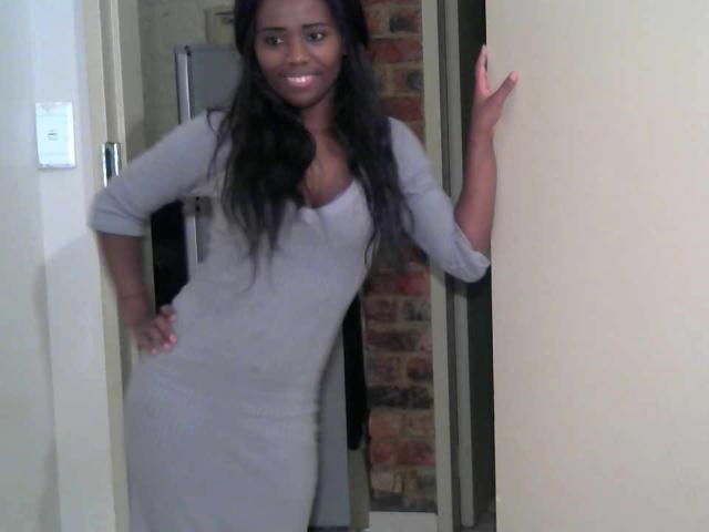 FatCreamyPussX with long black hair, smiling, wearing a tight gray dress, standing in a doorway, hand on hip, other hand on door, looking cute, dark skin, medium ass.