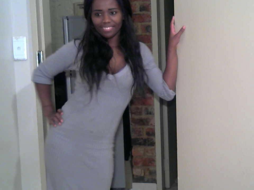 FatCreamyPussX with long black hair, smiling, wearing a tight gray dress, standing in a doorway, hand on hip, other hand on door, looking cute, dark skin, medium ass.