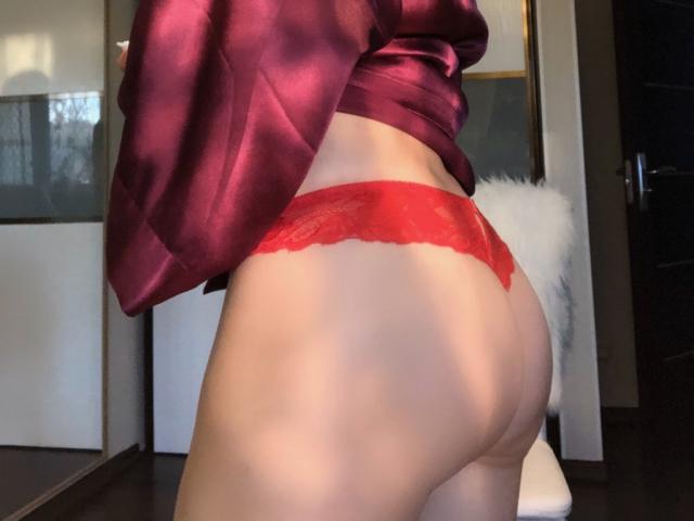 Il sedere scoperto di SugarLover, con biancheria intima di pizzo rossa, che mostra un piccolo sedere con pelle liscia e una parte bassa della schiena leggermente curva. Indossa una parte superiore di raso rosso lucido..