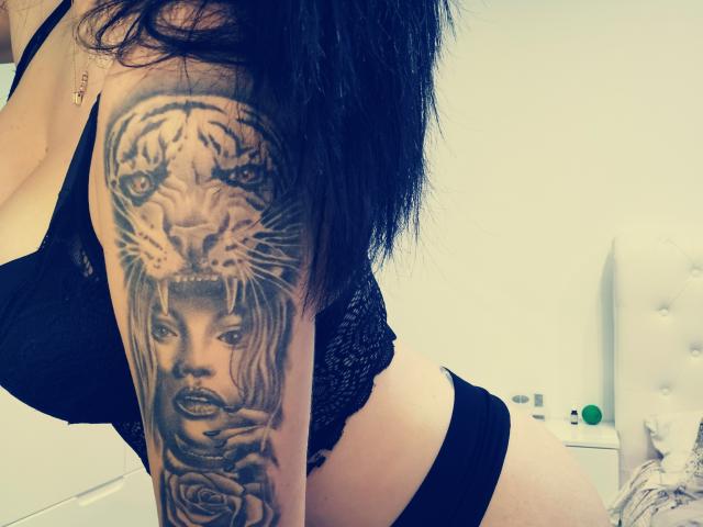 LovelyMichellex69 has a detailed black and gray tattoo of a tiger's face above a woman's face and roses on her right arm, wearing black lace lingerie and black panties.