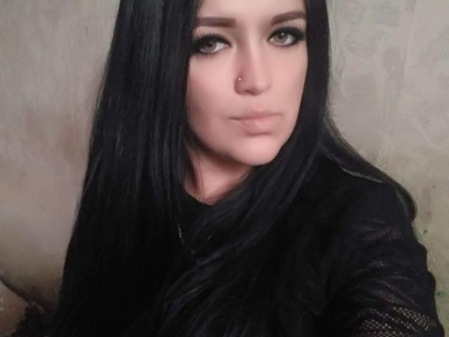 GavinGray with long black hair, green eyes, and a nose ring, wearing a black mesh top, looking serious. Boobs are not visible, focus is on her face.