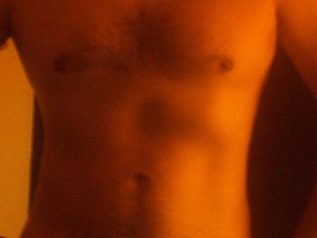 A blurry, orange-lit photo of GuapoHotAntonio's bare, slim, hairy-chested torso with small, dark nipples and a visible navel.