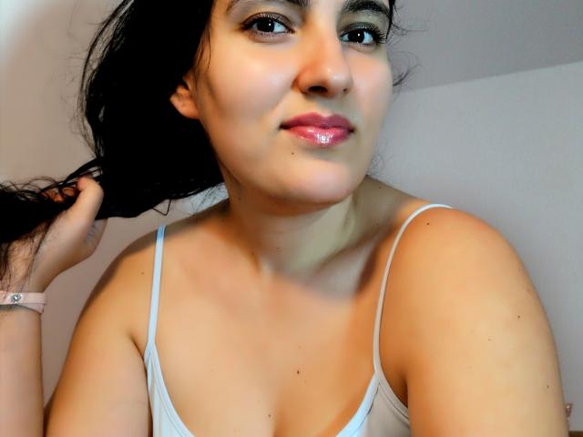 AddictedToUTS has shiny pink lips, light brown skin, black hair, and is wearing a white tank top, holding a hair strand, with a pink wristband.
