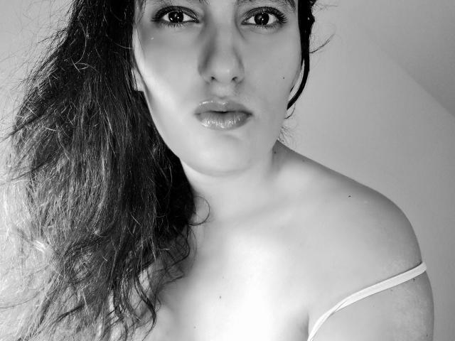 Black-and-white photo of AddictedToUTS with wet, wavy hair, glossy lips, and visible shoulder straps, looking straight at the camera, showing bare shoulders and a slight chest.