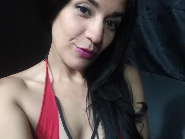 ValeryGirlLatin with long black hair, purple lipstick, and red halter top, showing her bare shoulders and cleavage, smiling subtly at the camera.