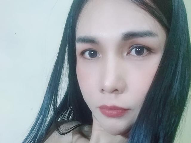 MissHotAyaLove has a pale face, black straight hair, brown eyes, and red lips with a serious expression, showing a cute, feminine, and attractive appearance.