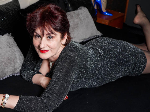 Alberta Allen, avec ses courts cheveux roux, allongée sur un lit noir, portant une robe noire scintillante, du rouge à lèvres rouge et des bas noirs, souriant à l'appareil photo, montrant ses fesses..