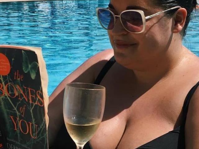 FoxDollBBW with large tits, dark hair, sunglasses, black bikini, holding book, and glass of white wine by the blue pool.