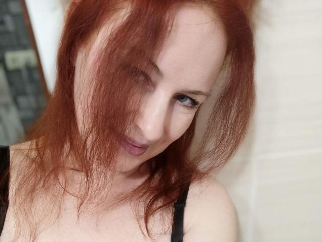 MarleneDavies with red hair, slightly messy, black strap top, fair skin, blue eyes, pouty lips, looking up, in a selfie. Boobs barely visible.