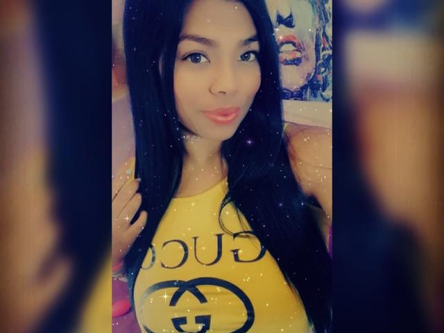 Sophiadiva with long black hair, yellow tank top, and pink lips, standing in front, blurred people on sides, sparkles overlay, cute, smiling softly, medium shot, realistic.