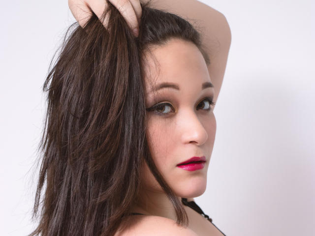 Mariana Rogers, con i capelli castano scuro raccolti, indossa un rossetto rosa, ha gli occhi marroni e un viso leggermente arrossato, e guarda oltre la spalla, mostrando la sua spalla nuda..