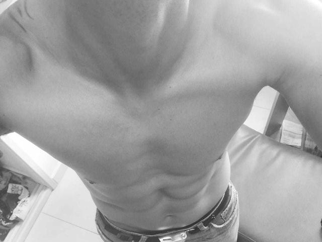 La parte superiore del corpo di VictorHotX, senza maglietta, mostra addominali definiti e costole visibili, indossa jeans sbottonati, con un piccolo tatuaggio sulla spalla destra, in una fotografia in bianco e nero..